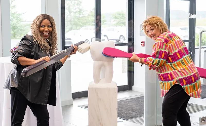 Erin Hendricks EFDA (left) and Tija Hunter brush a marble tooth sculpture in Benco Dental’s CenterPoint East showroom lobby;