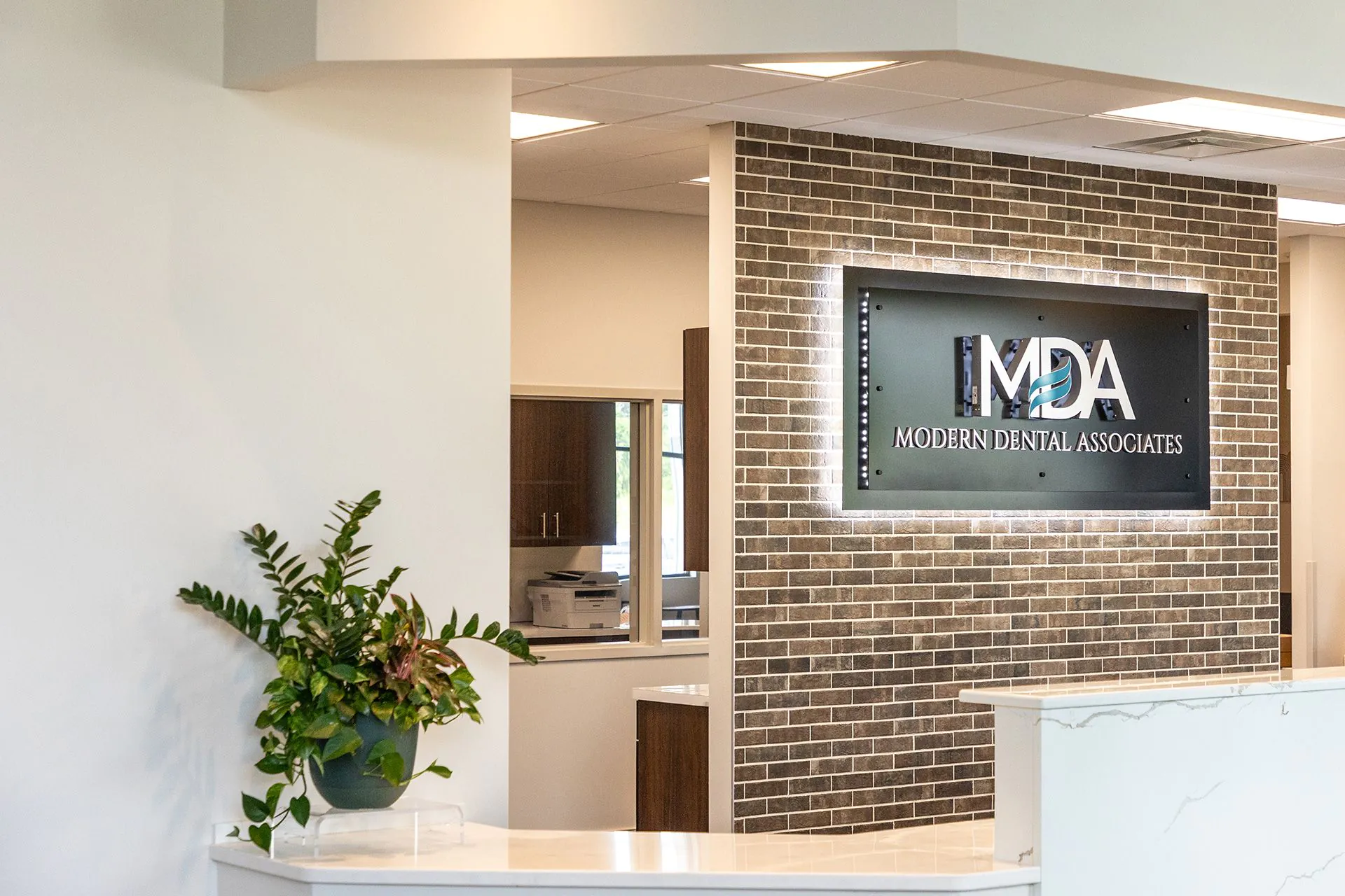 Warm welcome: “Dr. Parry wanted a bright space with whites and gray/beige tones with exposed brick and open ceiling, mid to dark wood tones, concrete, glass door and Midcentury Modern furniture,” says designer Amy Hnat.